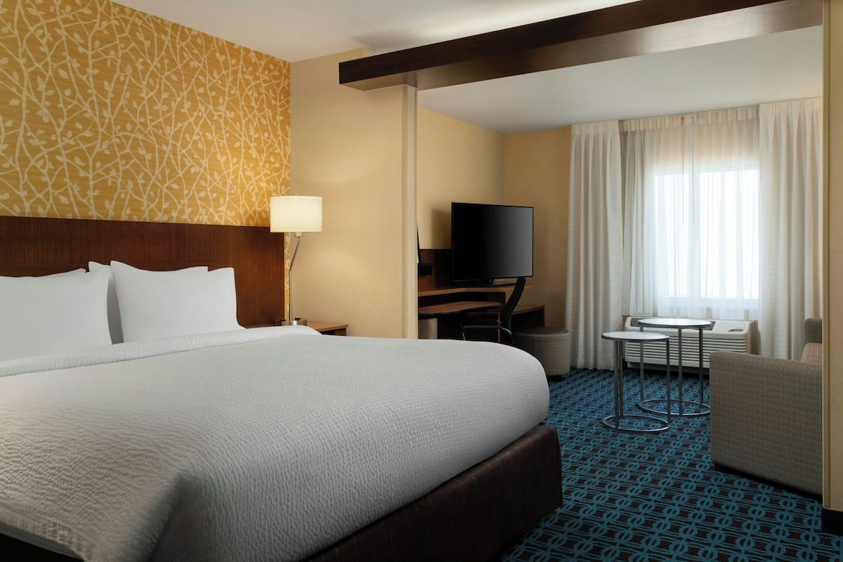 A hotel room with a large bed, a desk, a TV, and a small table.