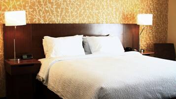 A hotel room with a large bed, two bedside tables with lamps, a nightstand, and a patterned wall.