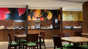 A restaurant with wooden tables and chairs, a counter with food items, and a mural with fruit and flowers. - Fairfield Inn & Suites by Marriott London (London)