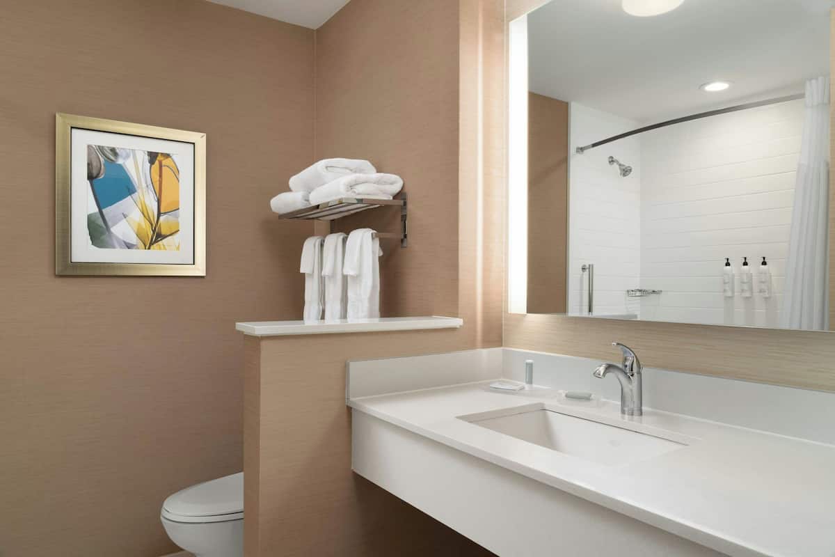 A modern bathroom with a white sink, a towel rack, and a framed artwork on the wall.