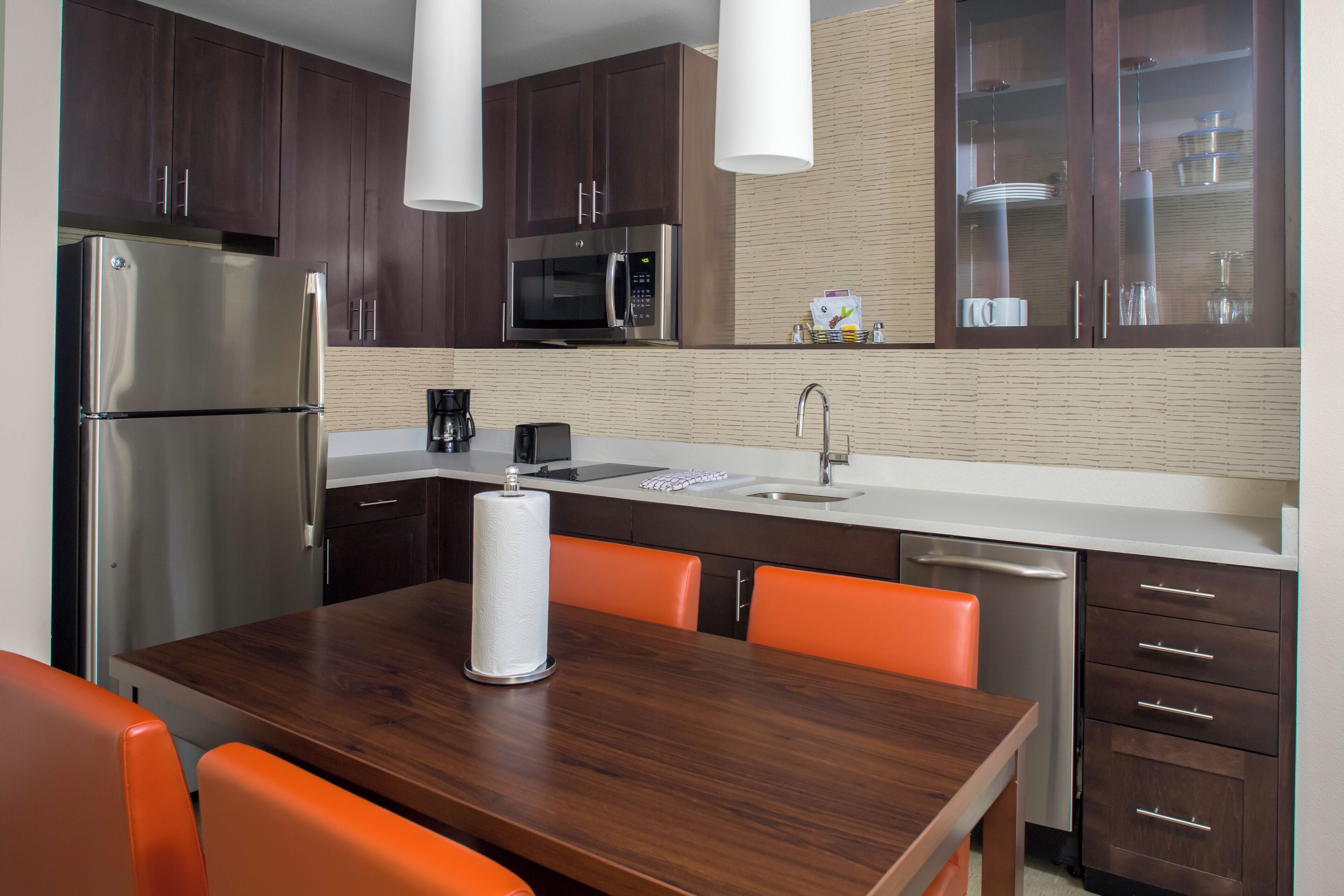 A modern kitchen with dark wood cabinets, stainless steel appliances, and orange chairs.