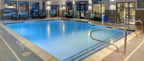 Una piscina interior con marcas de carriles claramente definidas, un elevador de piscina y zonas de estar con mesas y sillas.