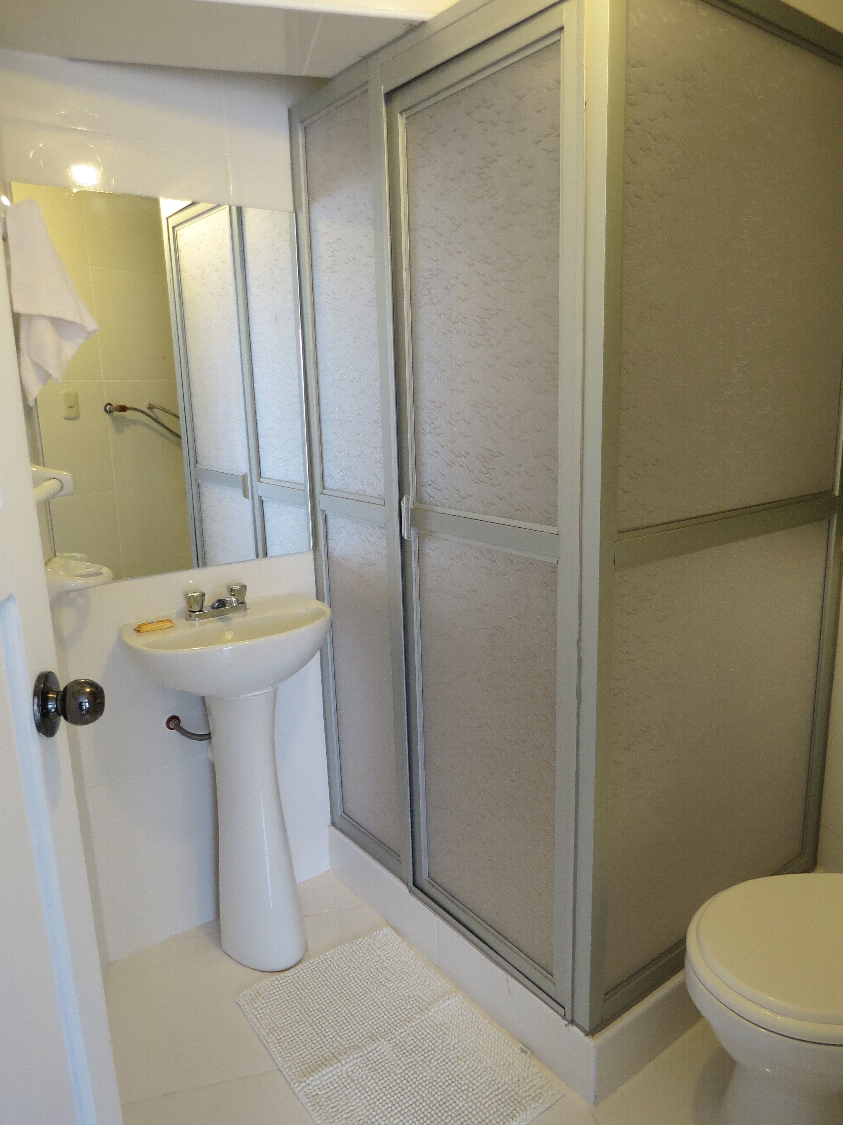 Un baño con lavamanos blanco, inodoro y cabina de ducha con paredes de vidrio.