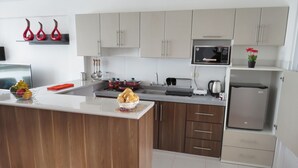 A modern kitchen with wooden cabinets, a stainless steel refrigerator, and a microwave. - Apartamentos Quewe (Cusco)