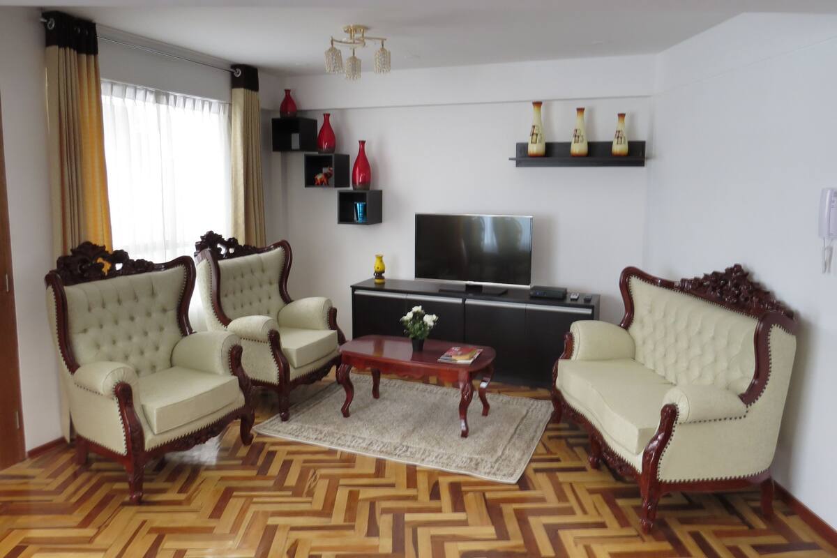 Un salon avec deux fauteuils, une table basse, un téléviseur et des objets décoratifs disposés sur des étagères.