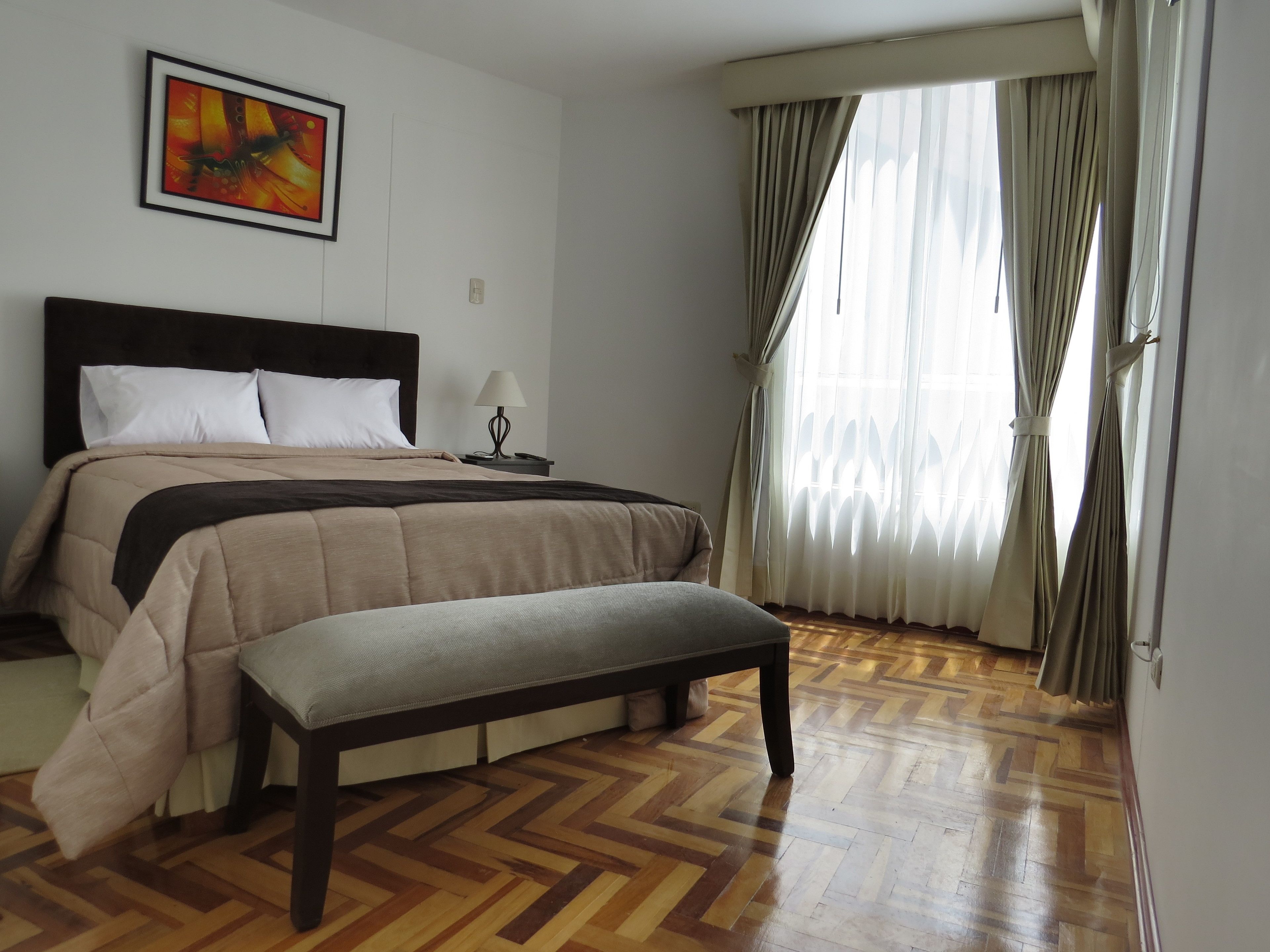 A neatly arranged bedroom with a bed, bedside table, lamp, and a bench.