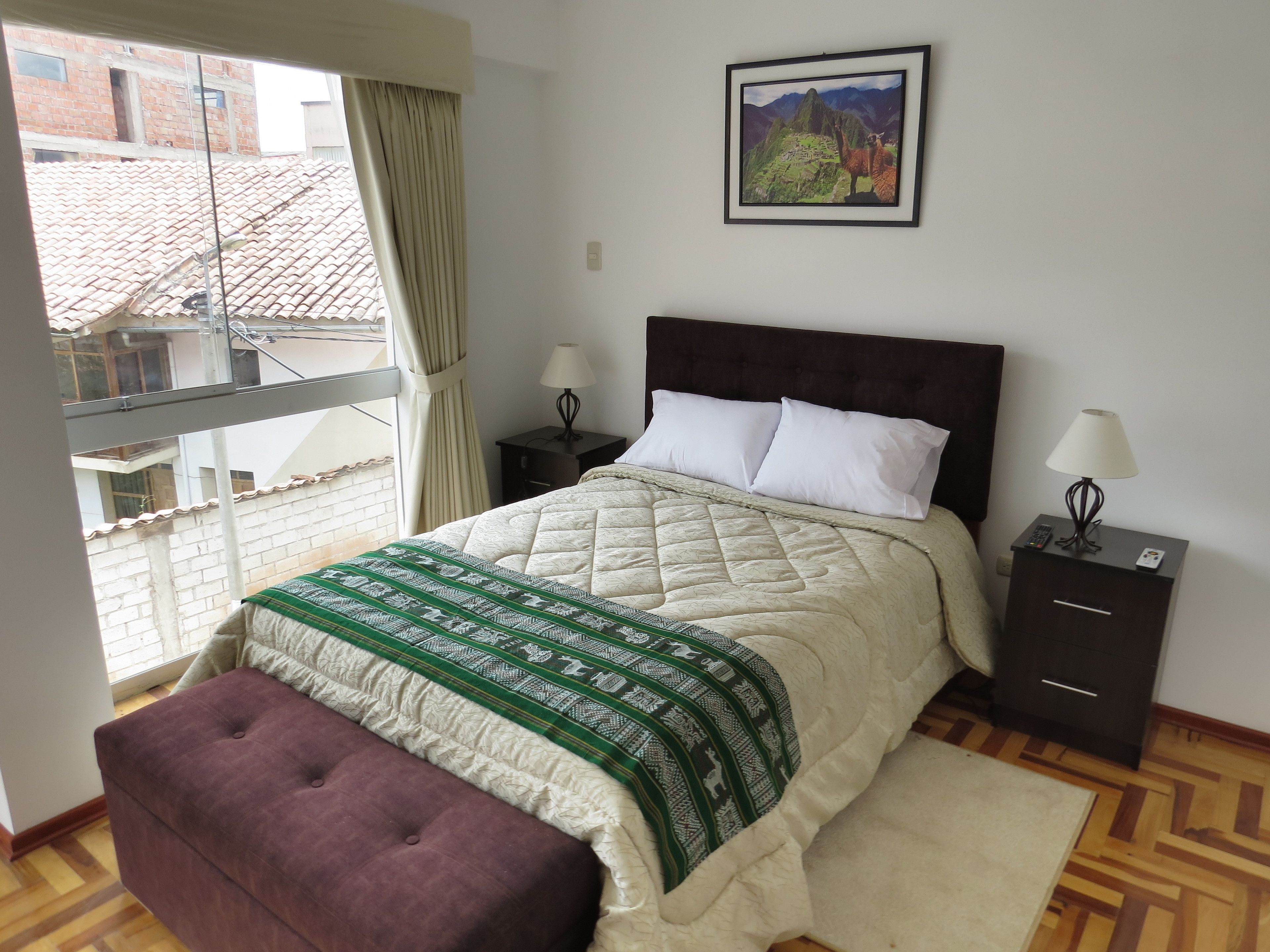 A bedroom with a bed, a nightstand, a lamp, a window with curtains, and a picture on the wall.