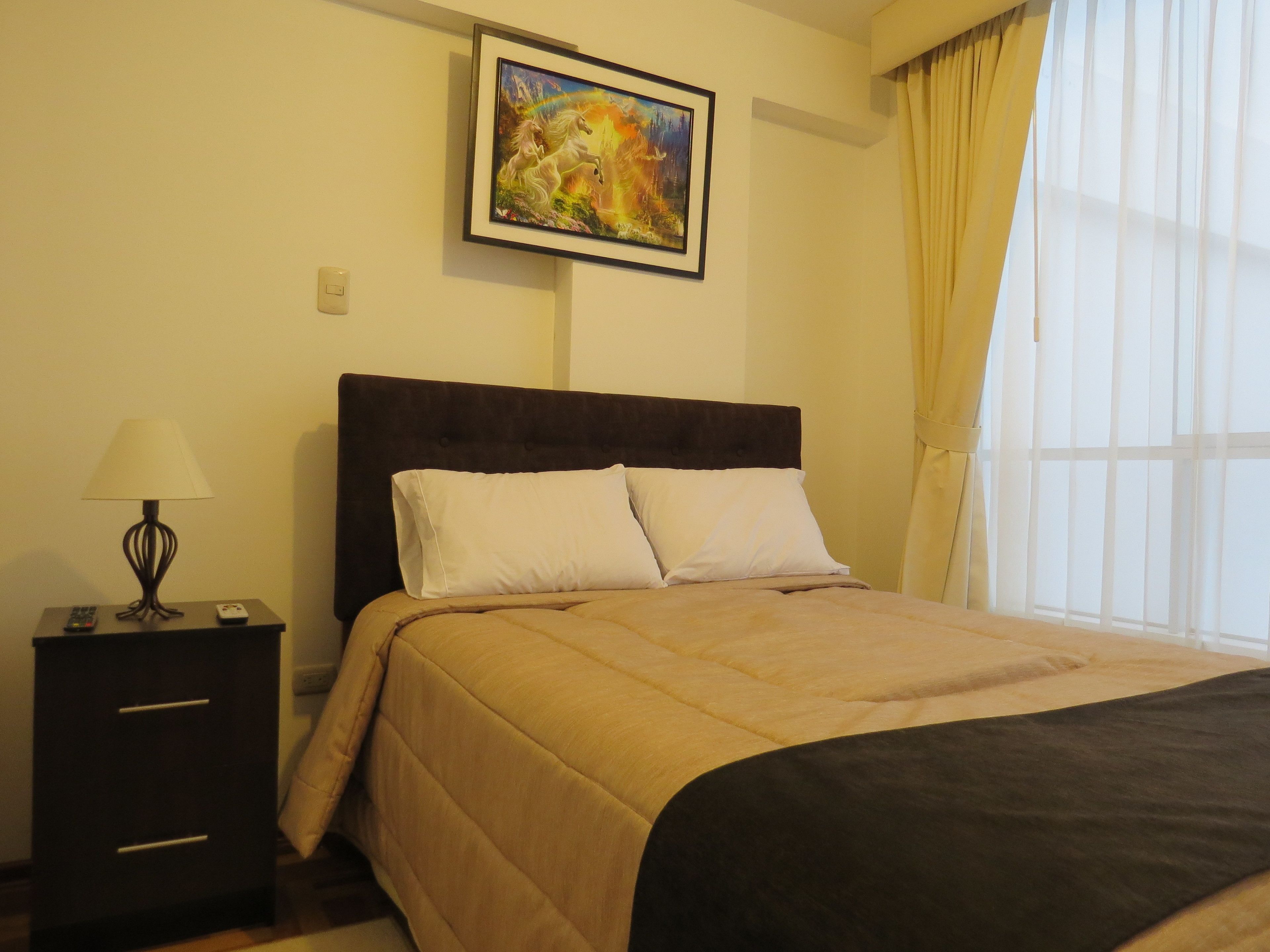 A neatly made bed with a dark headboard, a bedside table with a lamp, and a painting on the wall.