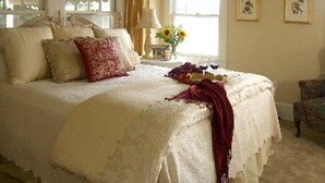 Un dormitorio con una cama grande, una mesita de noche con lámpara, una silla y dos cuadros en la pared.