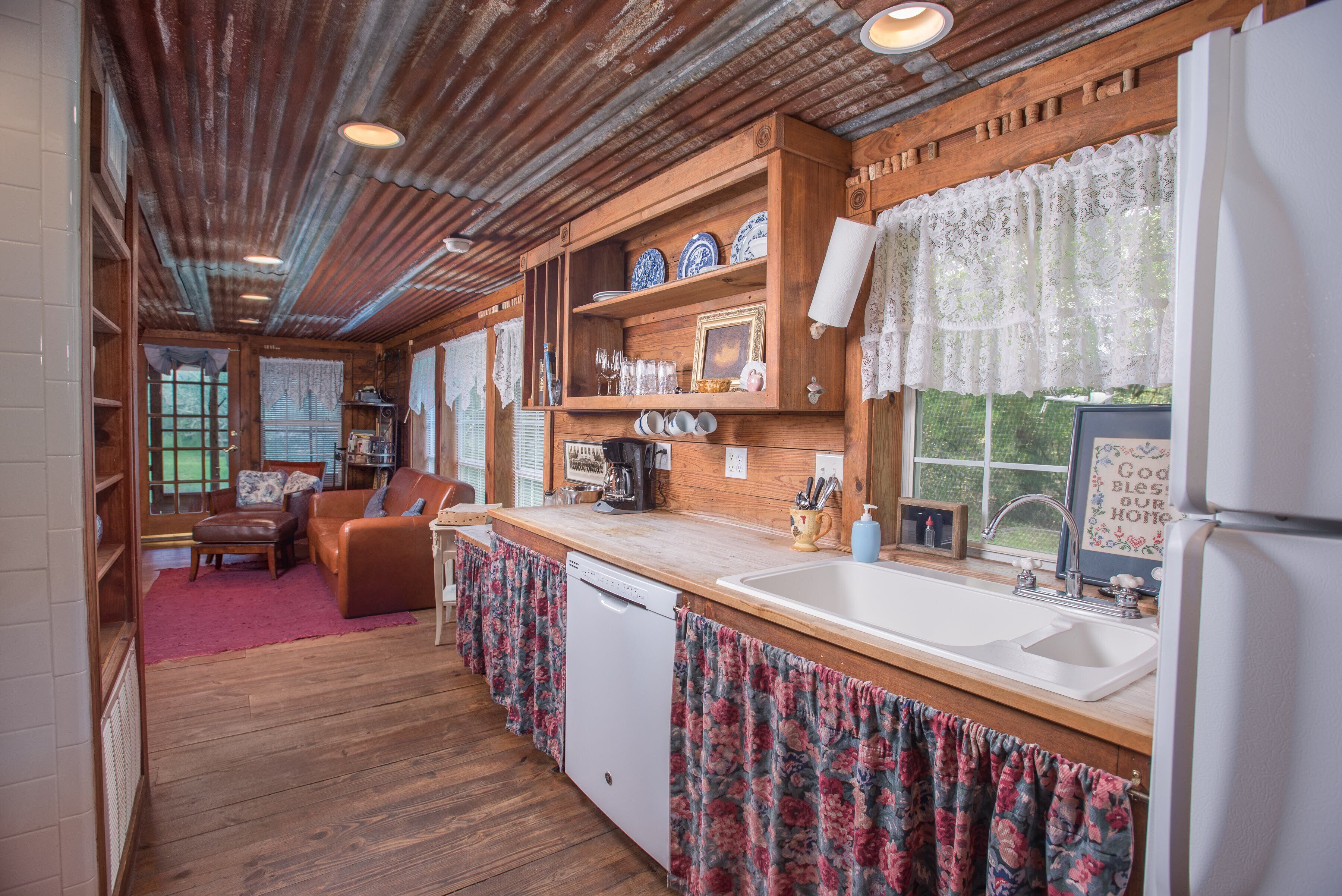 A kitchen with wooden cabinets, a dishwasher, a sink, and a window with lace curtains.