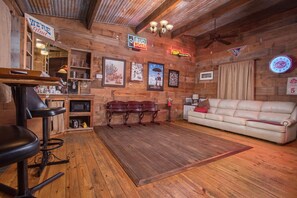 A rustic interior with wooden walls, a bar area, a sofa, and various framed pictures. - 7F Lodge (College Station)