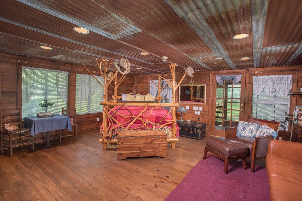A rustic cabin interior with a wooden bed, a table with a book, and a leather couch.