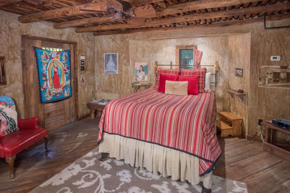 A rustic room with a wooden ceiling, a bed with a red and white striped bedspread, a red armchair, and a tapestry on the wall.