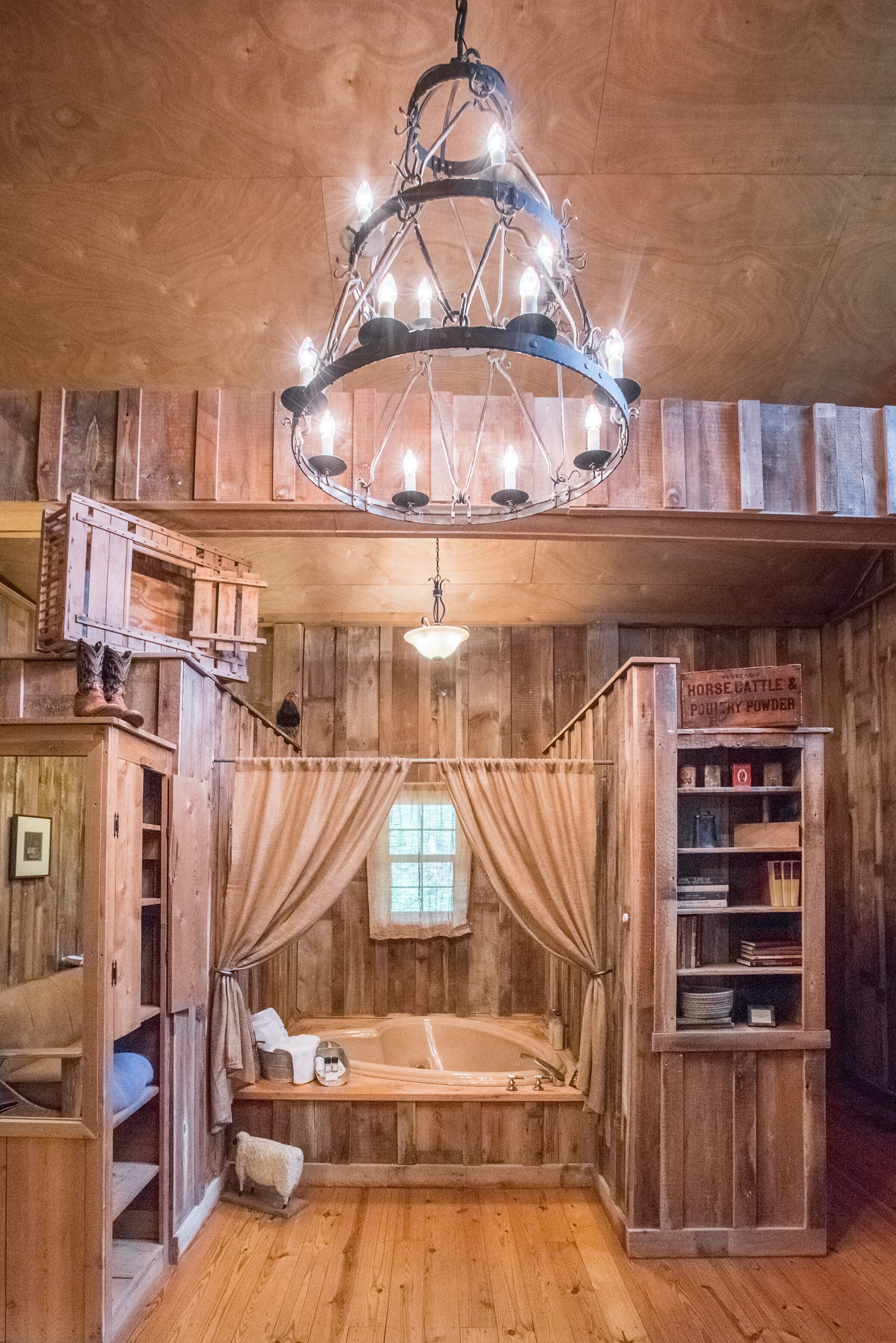A rustic wooden room with a canopy bed, a chandelier, and a shelf with books and a sign.