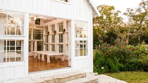 Un bâtiment en bois peint en blanc, doté de grandes fenêtres et d’une terrasse en bois.