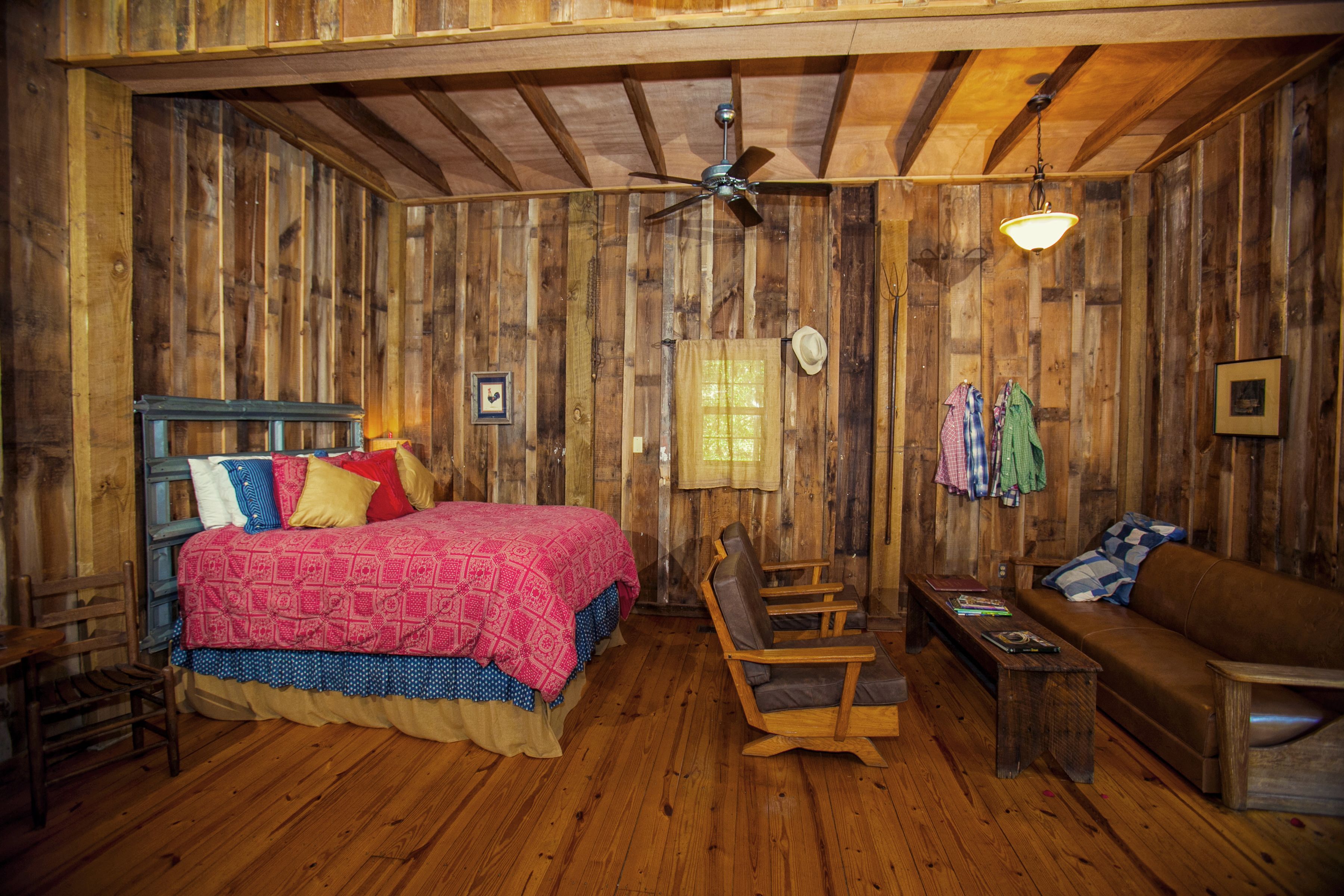 A rustic wooden room with a bed, a sofa, a chair, and a ceiling fan.