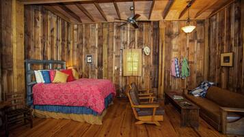 A rustic wooden room with a bed, a sofa, a chair, and a ceiling fan.