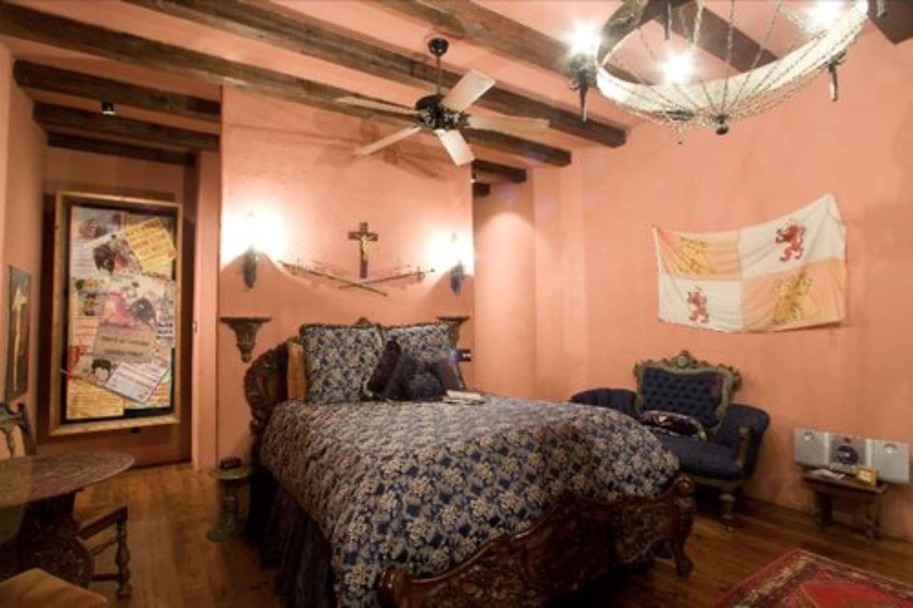 A bedroom with a wooden bed, a chair, a small table, a ceiling fan, and a wall-mounted light fixture.