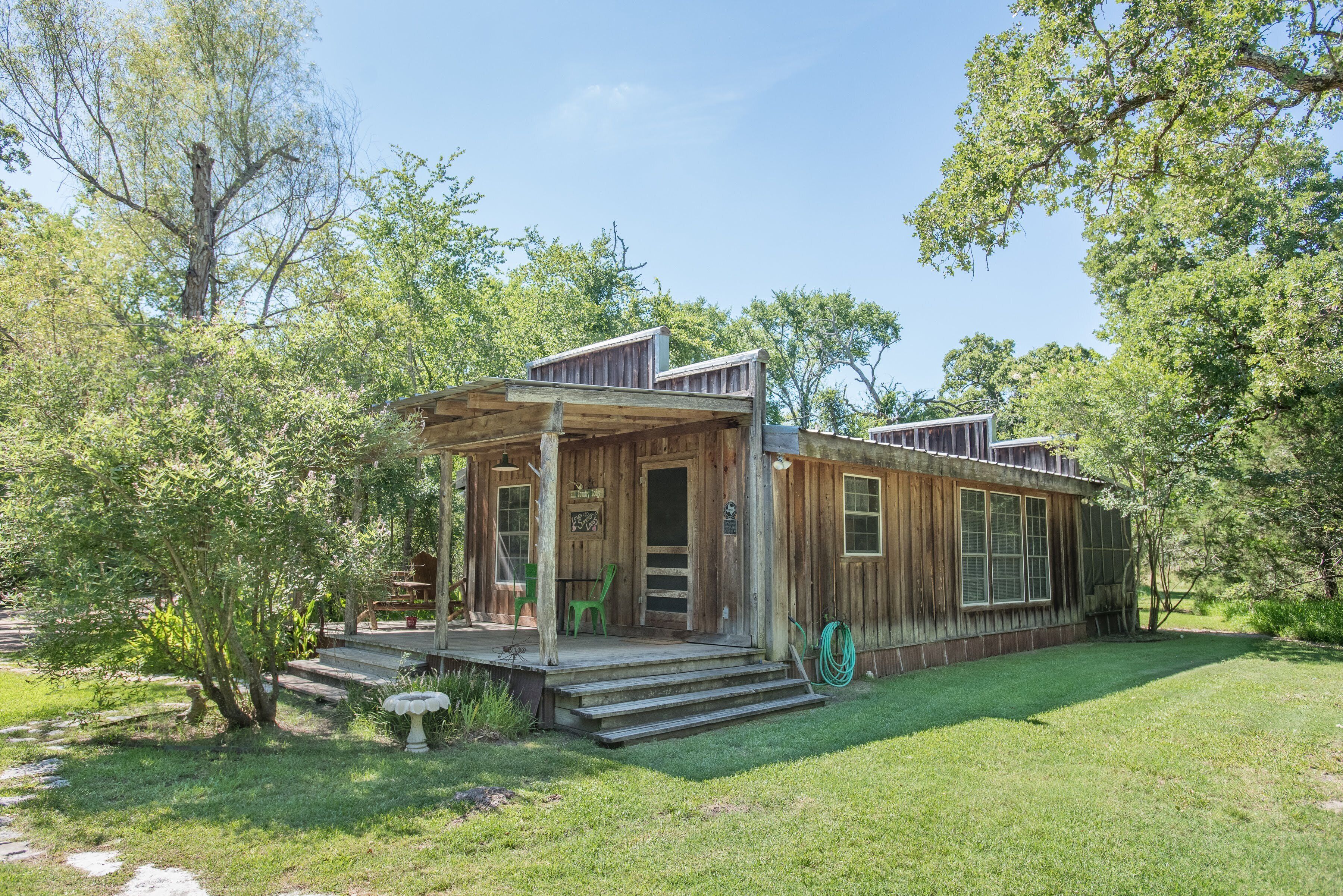 A rustic wooden cabin with a porch, surrounded by lush greenery and trees.