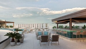 Un área de piscina en la azotea con sillones de descanso, un bar y vistas al océano.