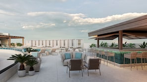 Un área de piscina en la azotea con sillones de descanso, un bar y vistas al océano.