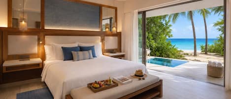 A modern bedroom with a large bed, a wooden headboard, and a view of a tropical beach and ocean.