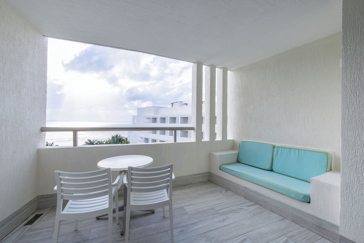 A balcony with a white table and chairs, a turquoise sofa, and a view of buildings.