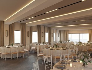 Un amplio salón de banquetes con varias mesas redondas, sillas blancas y una elegante decoración.