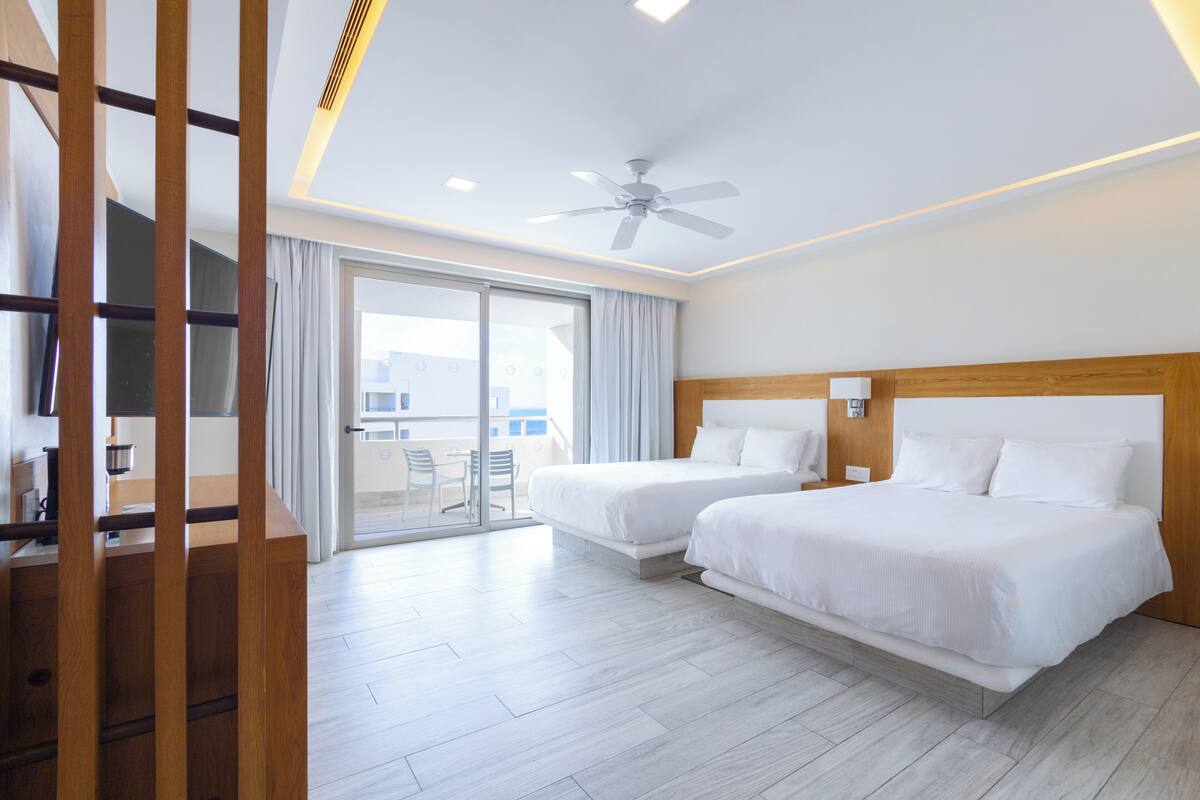 A hotel room with two beds, a ceiling fan, and a sliding glass door to the balcony.