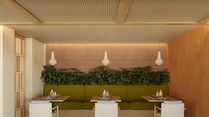 Un restaurante con una zona de asientos en cabina verde, mesas de madera e iluminación colgante.