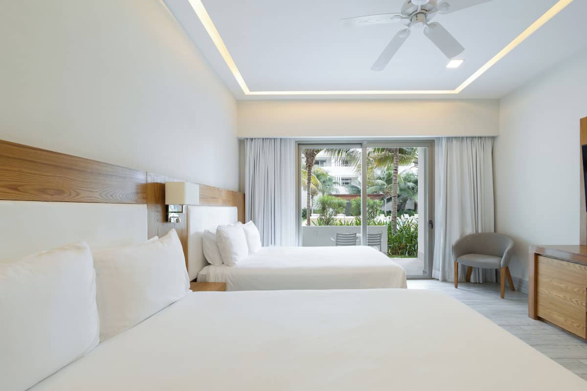 A hotel room with a large bed, a desk, a chair, a ceiling fan, and a view of the outdoors.