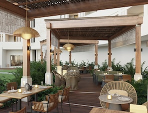 An outdoor dining area with wooden tables and chairs, surrounded by greenery. - Devossion By Live Aqua Celebration Resort & Spa Isla Mujeres (Isla Mujeres)