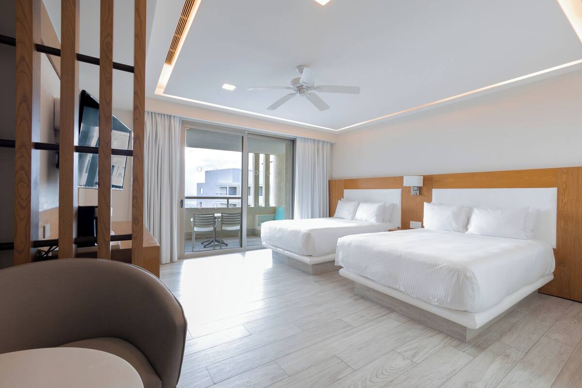 A hotel room with two beds, a ceiling fan, and a view of the city.