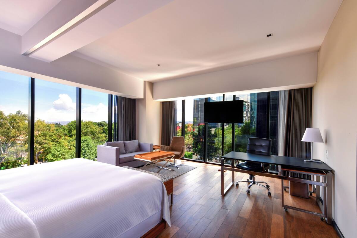A modern hotel room with a large bed, a desk, a sofa, and a TV.