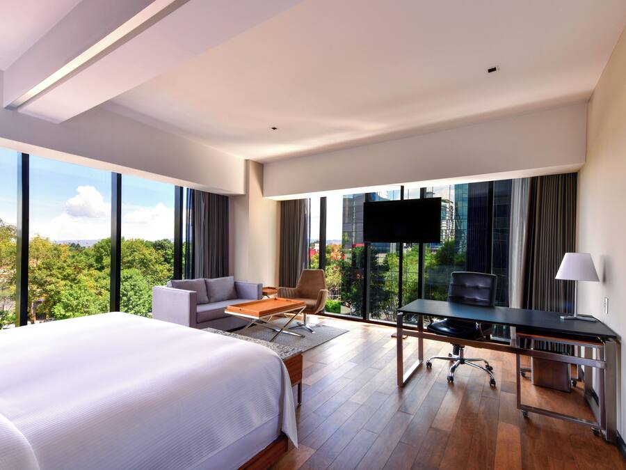 A modern hotel room with a large bed, a desk, a sofa, and a TV.