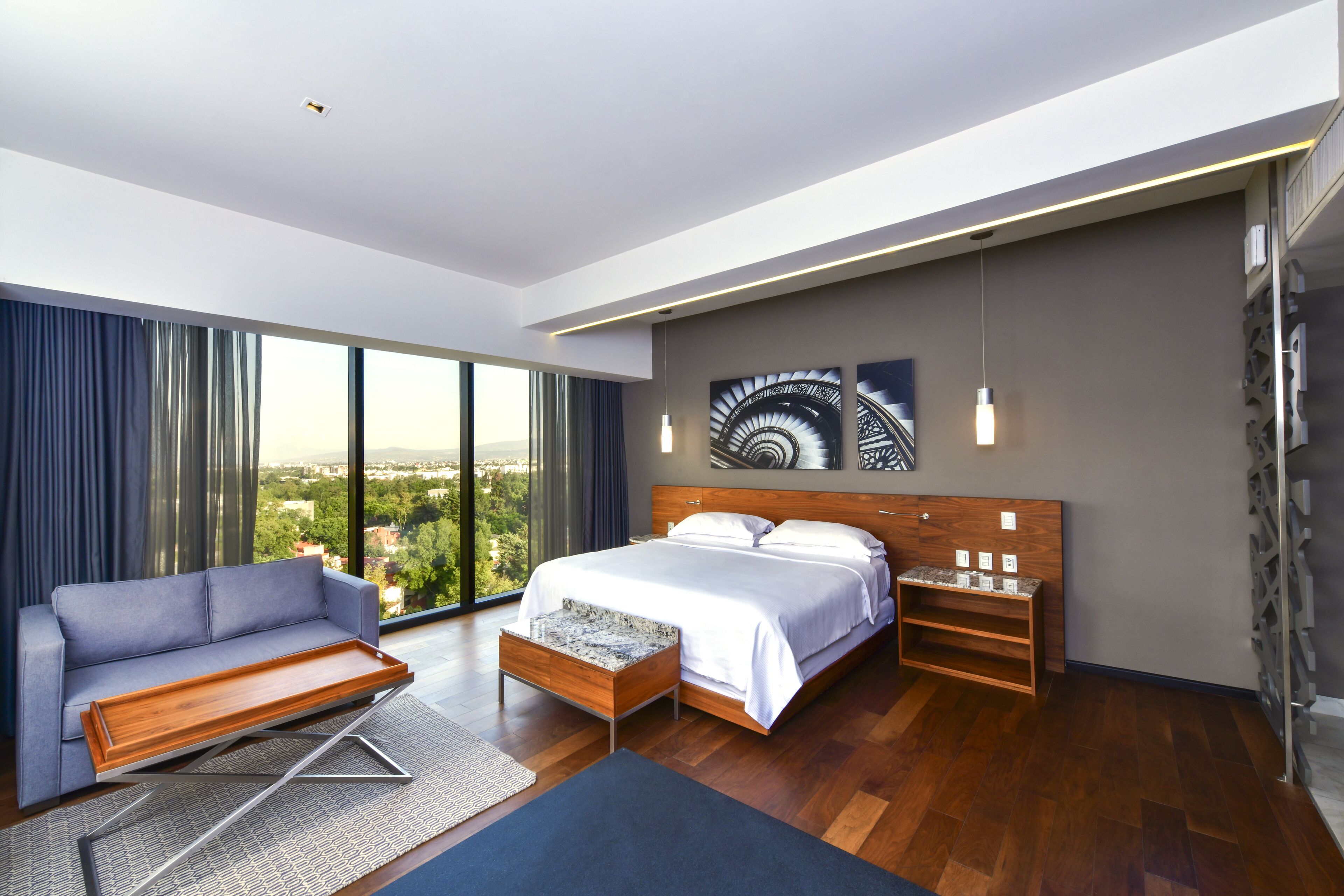 A modern hotel room with a large bed, a sofa, a small table, and a view of the city.