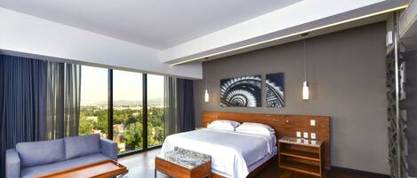 Una habitación de hotel moderna con una cama grande, un sofá, una mesita y vistas a la ciudad.