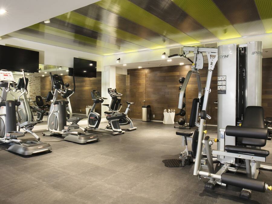 Un gimnasio con diferentes máquinas de ejercicio, incluyendo cintas de correr y estaciones de pesas, y un espejo grande.