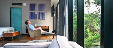 A modern hotel room with a large window, a bed, a sofa, and a coffee table.