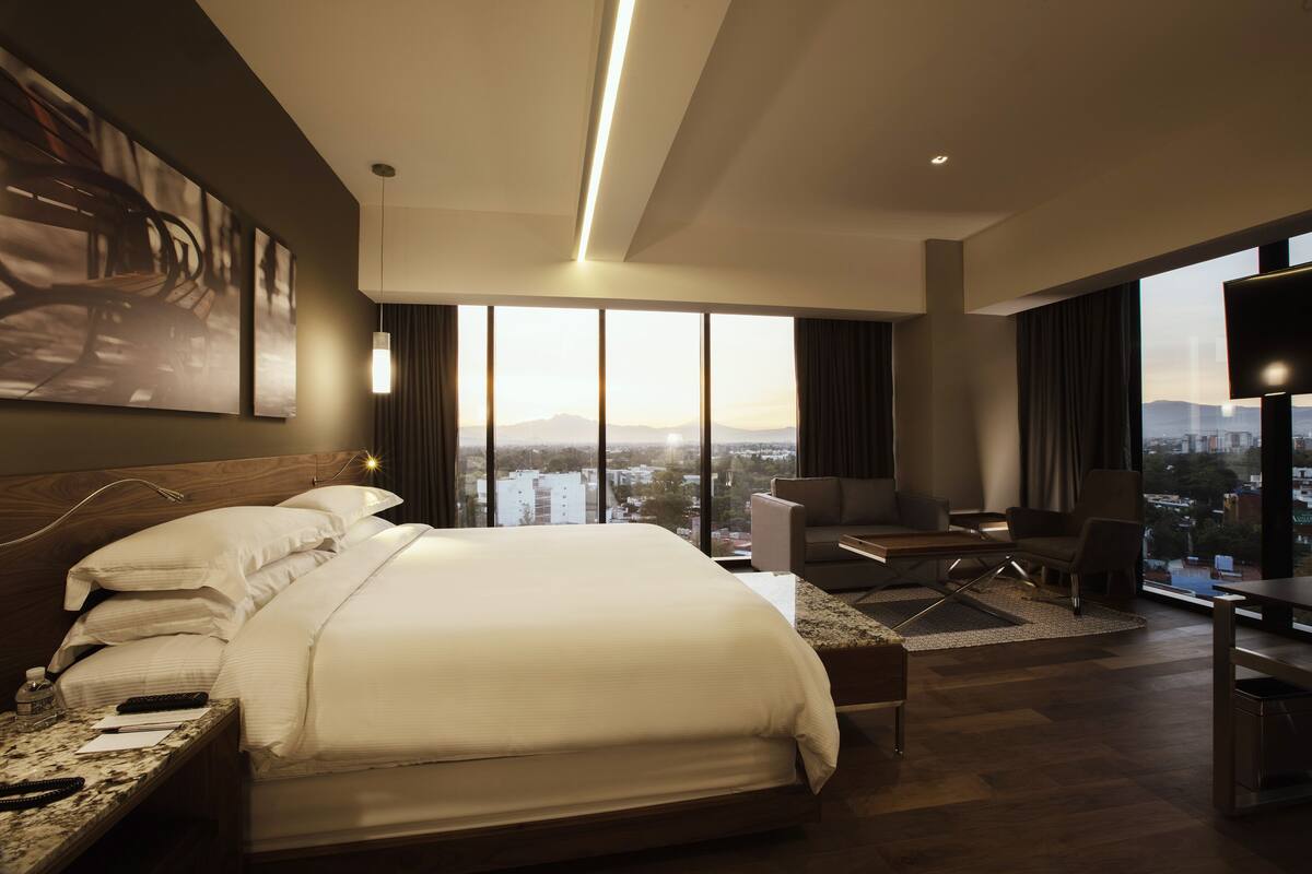 A modern hotel room with a large bed, a desk, and a view of the city.