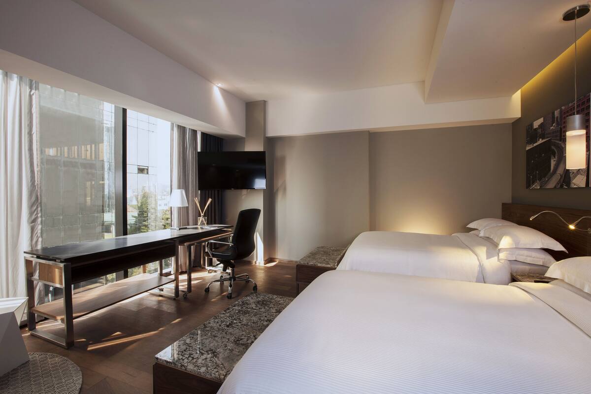 A modern hotel room with a large bed, a desk, and a chair.