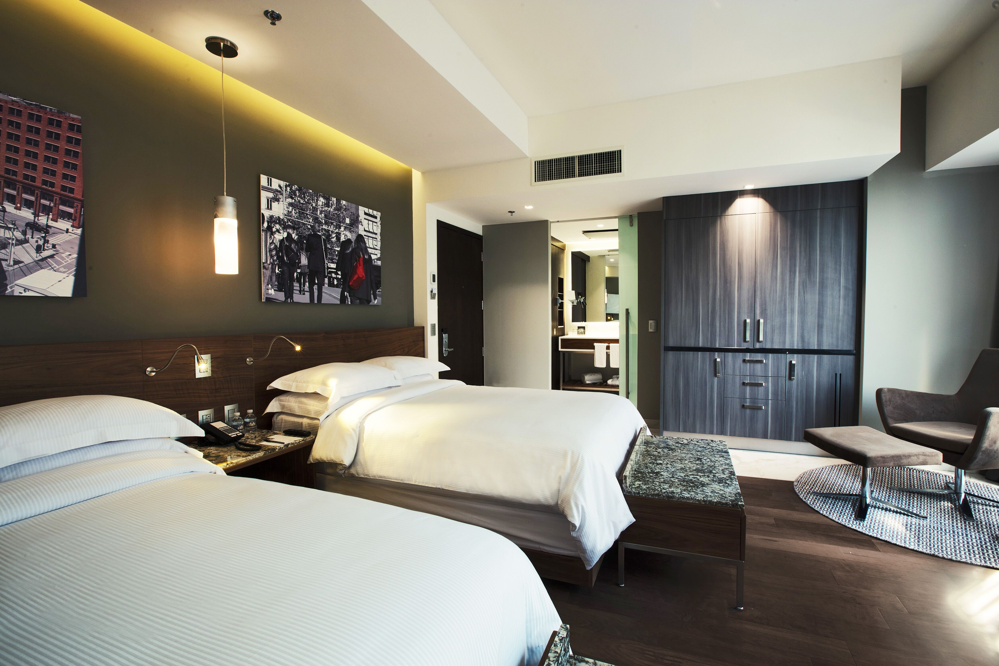 Ein modernes Hotelzimmer mit zwei Betten, einem Schreibtisch, einem Sessel und einem großen Kleiderschrank.