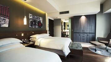 Ein modernes Hotelzimmer mit zwei Betten, einem Schreibtisch, einem Sessel und einem großen Kleiderschrank.