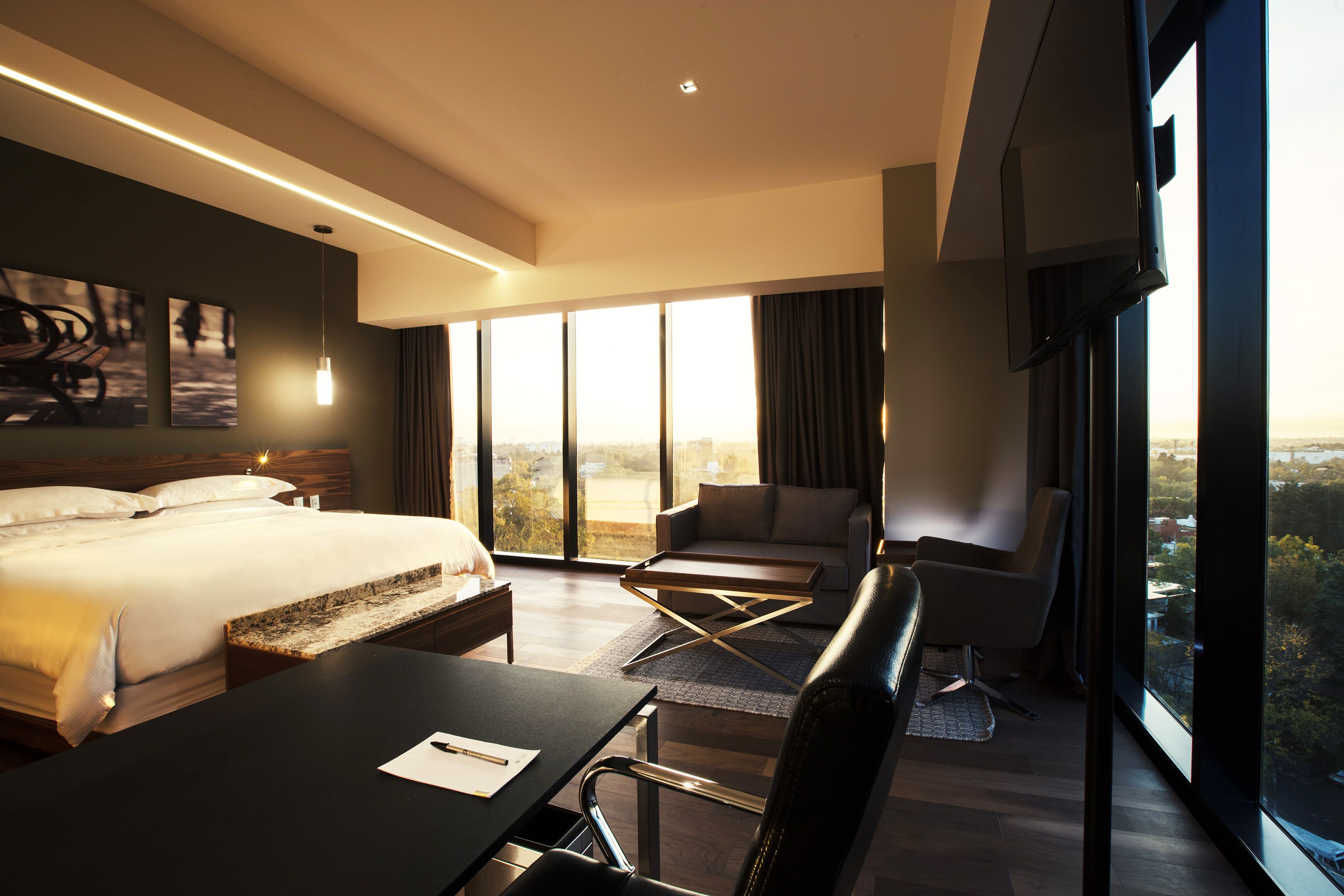 A modern hotel room with a large bed, a desk, a sofa, and a view of the city.