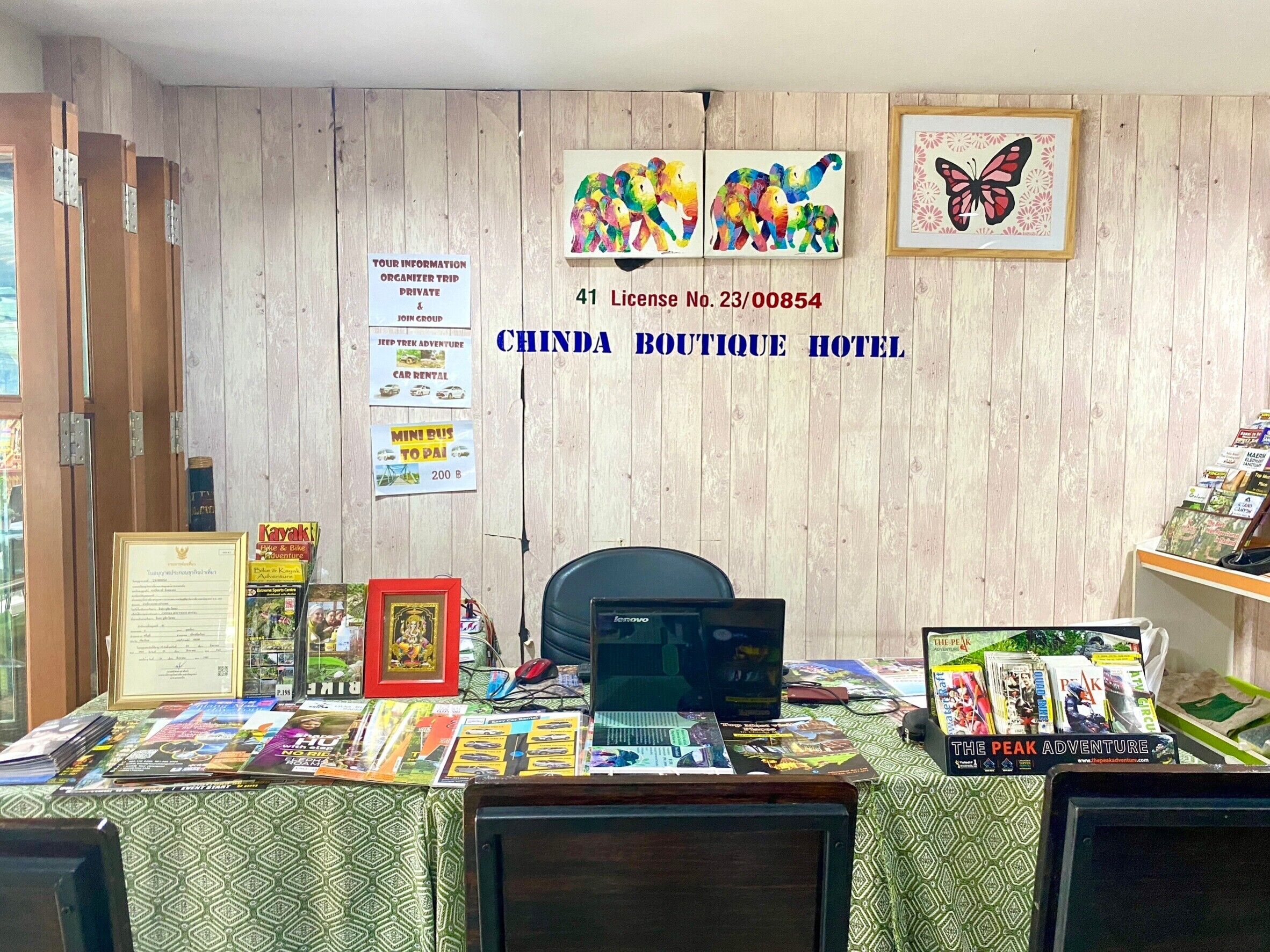 A reception desk at Chinda Boutique Hotel with a wooden wall, various signs, and a computer.