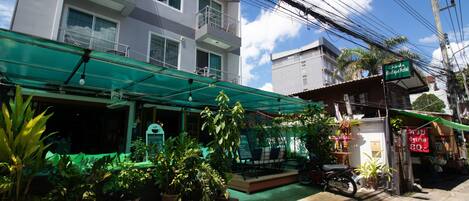 A hotel with a green awning, potted plants, and a motorcycle parked outside.