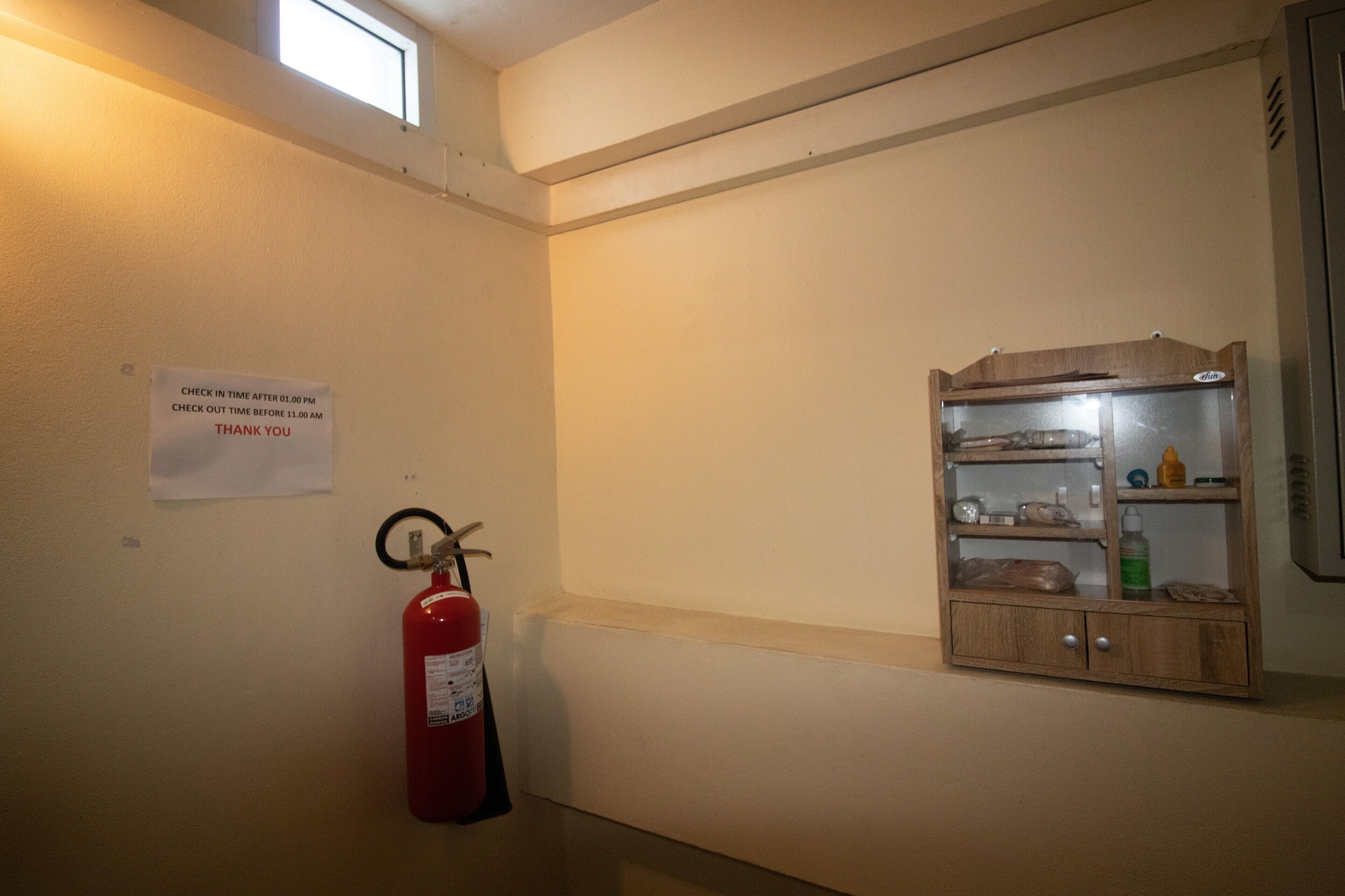A hallway with a fire extinguisher, a cabinet with shelves, and a sign indicating check-in and check-out times.