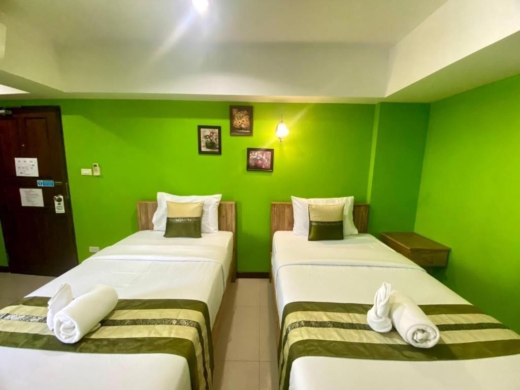 Une chambre d’hôtel avec deux lits, des murs verts et une petite table de chevet avec une lampe.