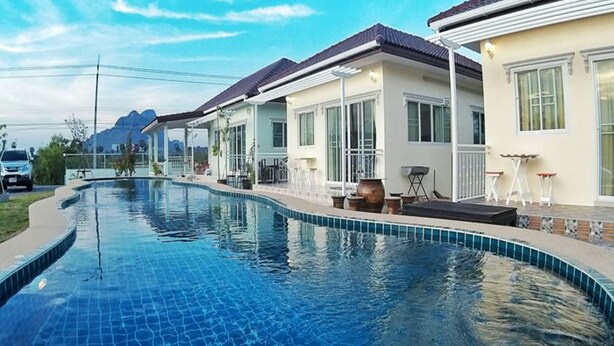 A swimming pool with a tiled edge, surrounded by houses with white walls and dark roofs. - Sky & Water (Cha-am)