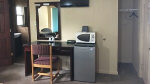 Une pièce de taille modeste équipée d’un bureau, d’une chaise, d’un four à micro-ondes et d’un téléviseur fixé au mur.
